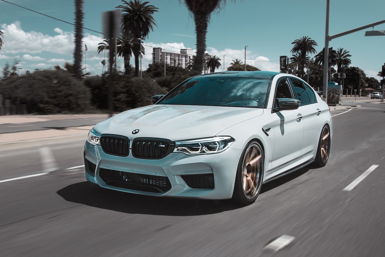 Светлый BMW M5 Competition на приморской улице среди пальм