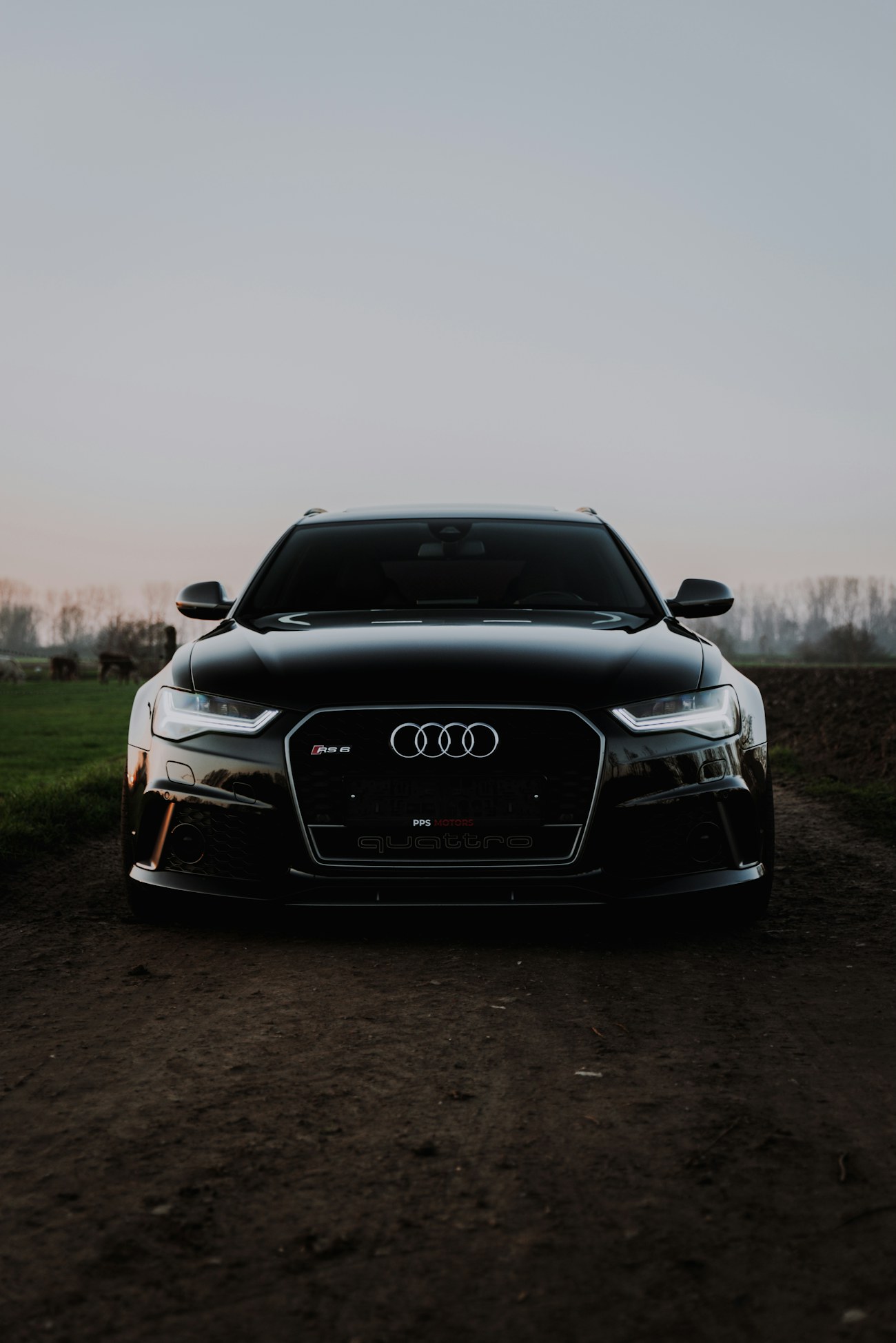 Чёрный Audi RS6 Avant анфас на просёлочной дороге в сумерках